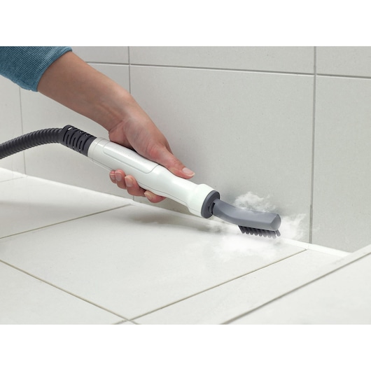 BLACKDECKER FSMHBA steam cleaner brush cleaning grout between white tiles, hand holding handle.