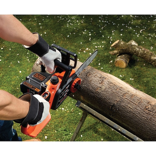 BLACKDECKER GKC1825L20 cordless chainsaw cutting log outdoors, close-up view of tool in use.