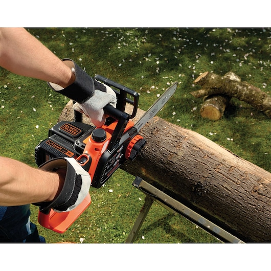 BLACK+DECKER GKC3630L20 chainsaw cutting a large tree branch outdoors, close-up of hands and tool in use.