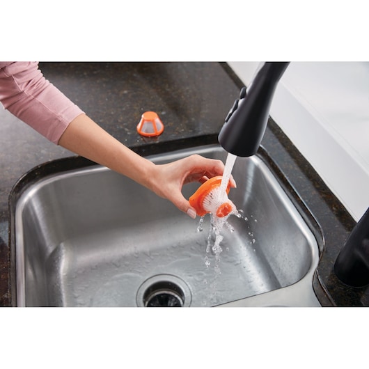BLACKDECKER HLVC315J11 orange brush filter being rinsed under tap in kitchen sink, photography