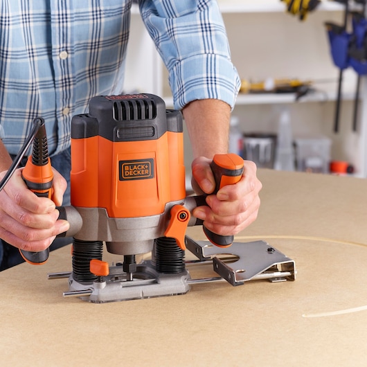 Photo of BLACK+DECKER KW1200EKA plunge router in use on wood, close-up view, user holding both handles.