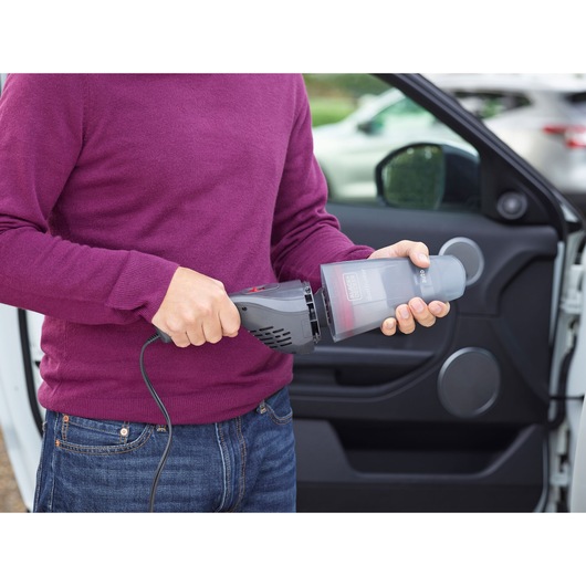 BLACKDECKER NVB12AVA handheld vacuum cleaner with dust container, shown during car cleaning.