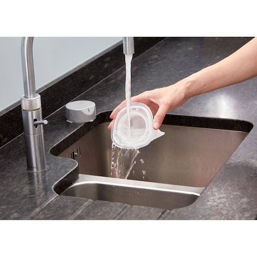 BLACKDECKER NVC115W vacuum filter being washed under running water in a kitchen sink.