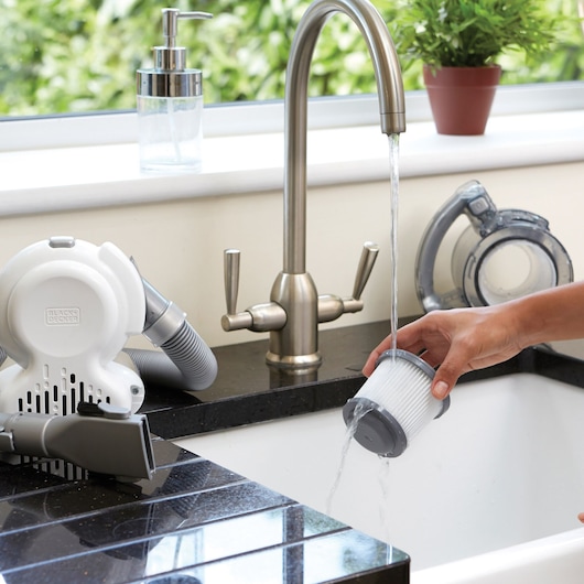 BLACK+DECKER PD1820L handheld vacuum filter being rinsed under faucet in kitchen sink, close-up.