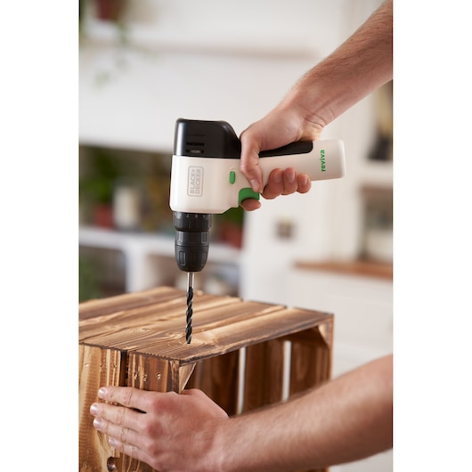 Photo of BLACK+DECKER REVDD12C cordless drill being used to drill into a wooden crate indoors.