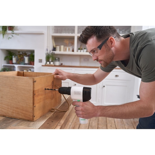 BLACKDECKER REVDD12C cordless drill used on wooden box in kitchen setting.