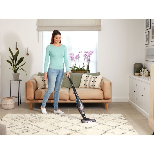 Photo of a person vacuuming a rug in a living room with a BLACK+DECKER SVB620JW cordless stick vacuum cleaner.