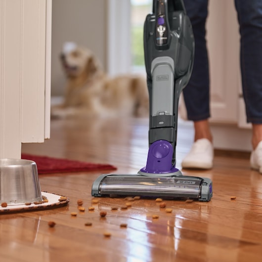 Photo of BLACKDECKER SVJ520BFSP stick vacuum cleaning pet food from hardwood floor near a dog bowl indoors.