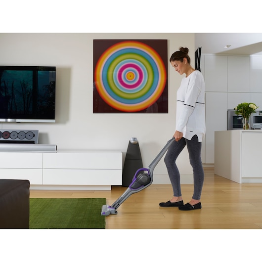BLACKDECKER SVJ520BFSP cordless stick vacuum in use on hardwood and green rug in modern living room.