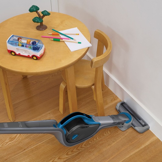 BLACKDECKER SVJ520BFS cordless stick vacuum cleaning wood floor near round table and chair, side view.