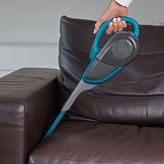 BLACKDECKER SVJ520BFS handheld vacuum cleaning brown leather sofa corner.
